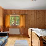 Schlafzimmer mit Holzwand, Bett, Sofa und Fenster mit Vorhängen.