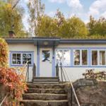 Ein Haus mit blauen Fensterrahmen und weißer Tür. Treppen führen zur Eingangstür.