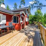 Rotes Haus mit Holzterrasse, Tisch und Stühlen, umgeben von Bäumen.