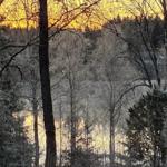 Schneebedeckte Bäume umgeben einen See bei Sonnenuntergang.