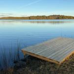Holzterrasse am ruhigen Seeufer mit Blick auf Wald und Wasser.