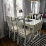 Esszimmer mit weißem Tisch und Stühlen, Fenster mit Vorhängen, Sofa im Hintergrund.