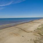 Weitläufiger Strand mit sandigem Ufer und blauem Meer unter klarem Himmel.