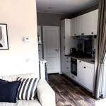 Wohnzimmer mit Sofa, Küchenbereich und Fenster mit Vorhängen.