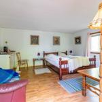 Ein Schlafzimmer mit Bett, Tisch, Stuhl und Küchenzeile. Holzboden und Fenster mit Vorhängen.