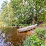 Ein kleines Boot liegt am Ufer eines Sees, umgeben von Bäumen und Gras.