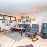 Wohnzimmer mit Sofa, Sessel und Kaminofen. Holzboden und Fenster mit Buntglas.