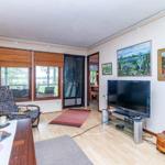Wohnzimmer mit TV, Fenstern und Gemälden an der Wand.