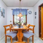 Esszimmer mit Holztisch, vier Stühlen und Fenster mit blau-weißem Vorhang.