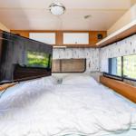Schlafzimmer mit Bett, TV und Fenstern.