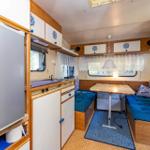 Küche mit Kühlschrank, Tisch und Sitzbank mit blauen Kissen.