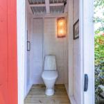 Hinter einem roten Tor befindet sich eine Toilette mit Holzboden und einer Wandlampe.