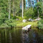 Holzsteg führt zu einem ruhigen See im Wald mit Bäumen und Felsen.
