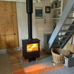 Kaminofen mit brennendem Feuer, Holztreppe und Korb im Raum.