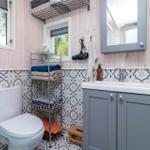 Badezimmer mit Toilette, Waschbecken und Badewannenbereich. Holzwände und Mosaikfliesen.