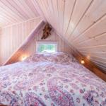 Schlafzimmer mit Holzwand und Dachschrägen, Bett mit Muster, Fenster und Wandlampe.