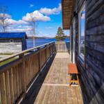 Holzterrasse mit Blick auf See und Himmel. Holzbank und Fenster sichtbar.