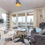 Wohnzimmer mit Sofa, Stühlen und TV. Balkon mit Sicht auf Wald.