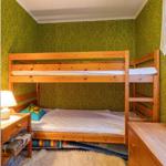 Zimmer mit Holz-Etagenbett, grünem Tapeten und Nachttisch mit Lampe.
