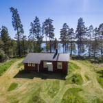 Rotes Holzhaus mit Dach im Wald, See im Hintergrund.