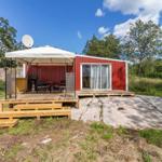 Rotes Gartenhaus mit Terrasse, Sonnenschutz und Satellitenanlage.