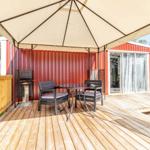 Terrasse mit Pavillon, Tisch, Stühlen und Grill. Rotes Gebäude mit Glasfront.
