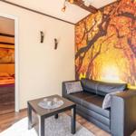 Wohnbereich mit Sofa und Tisch. Wandtapete mit Baummotiv. Tür zum Schlafzimmer.