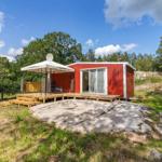 Rotes Holzhaus mit Terrasse und Sonnensegel in grüner Umgebung.