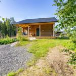 Wooden cabin with porch, surrounded by forest and greenery.