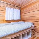 Bedroom with wooden walls, bed, and window with white curtains.