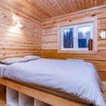 Bedroom with wooden walls, bed, and window with view of forest.