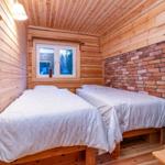 Two beds in a room with wood wall and brick wall.