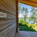 Wooden house with sign RATZERLITZ and view of lake and trees.