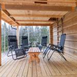 Wooden terrace with four lounge chairs and table. View of forest in background.