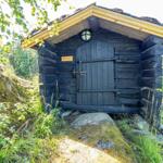 Wooden sauna with sliding door and roof, surrounded by grass and trees.