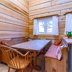 Dining area with wooden table, bench seating, and windows with white curtains.