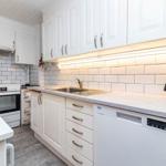 Küche mit weißen Schränken, Spüle und Kochfeld. Hintergrund ist Fliesenspiegel.
