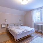 Schlafzimmer mit Bett, Holzboden und Fenster mit Blick auf Bäume.
