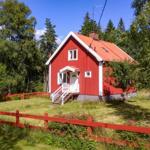 Rotes Holzhaus mit weißen Fensterrahmen und rotem Zaun im Grünen.