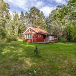 Red wooden house with terrace in the woods. Lawn and trees surround the accommodation.