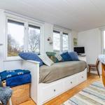 Schlafzimmer mit Bett, Fenstern und Stuhl. Holzboden und weiße Wände.