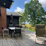 Terrasse mit Tisch, Stühlen und Liegestuhl. Blick auf Felder und Bäume.