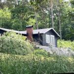 Schwarze Holzhütte mit rotem Schornstein im Wald. Eingangstreppe und Fenster mit weißen Rahmen.