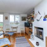 Wohnzimmer mit Kamin, Fenstern und Holzboden. Möbel und Dekoration sind sichtbar.