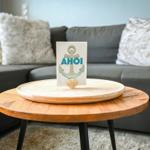 Ein runder Holztisch mit einer Karte und einer Muschel. Hintergrund: Sofa mit Kissen.