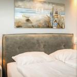 Ein Bett mit weißer Bettwäsche und einem grauen Kopfteil. Über dem Bett hängt ein Strandgemälde.