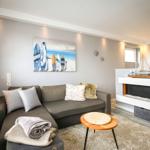 Wohnzimmer mit Sofa, Kamin und Wandbildern mit Surfbrettern und Segelbooten.