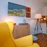 Ein Raum mit gelbem Sessel, Küchenbereich und Wandbild.