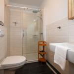 Badezimmer mit Dusche, Waschbecken und Toilette. Holzregal und Handtuch.