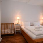 Schlafzimmer mit Bett, Kinderbett und zwei Nachttischen mit Lampen.